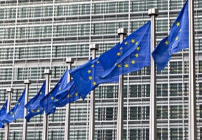 Image du siège de l’Union européenne à Bruxelles, derrière une rangée de drapeaux de l’Europe.